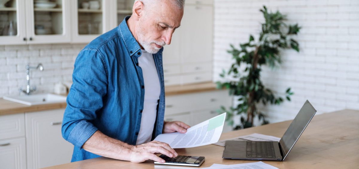 a man at his laptop reviewing electricity bill papers